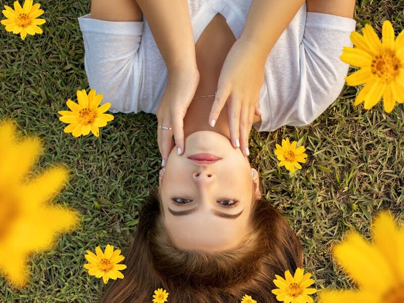 Upside down portrait of a woman lying on grass with yellow flowers in her hair.