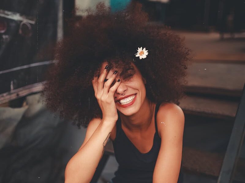 Cheerful woman wearing ripped jeans and curly hair with flower, enjoying a sunny day outdoors.