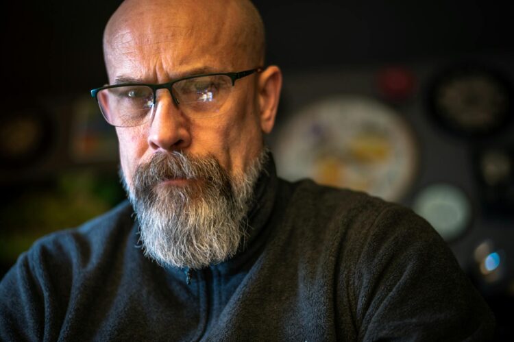 Close-up of a bald man with glasses, serious expression, indoors