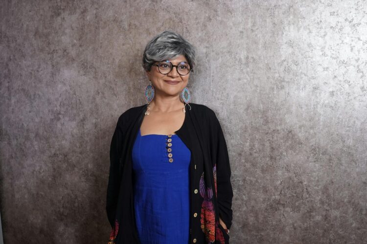 Portrait of a senior woman with gray hair wearing a blue dress and glasses, exuding confidence and elegance.