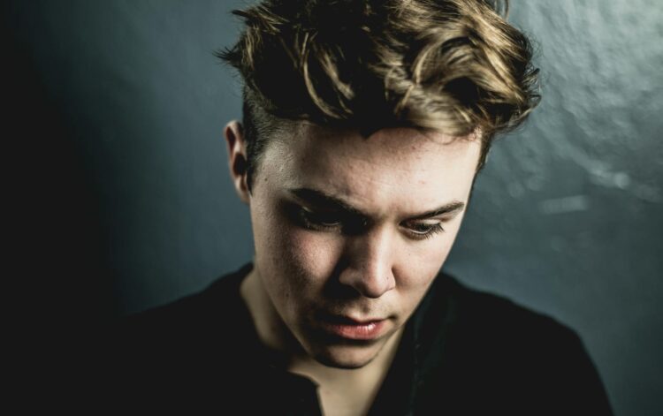 Close-up portrait of a young man with a thoughtful expression against a dark background.