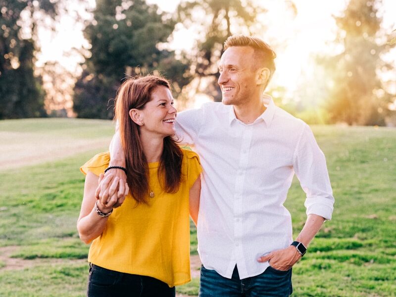 man in white dress shirt and woman in orange long sleeve shirt standing on green grass
