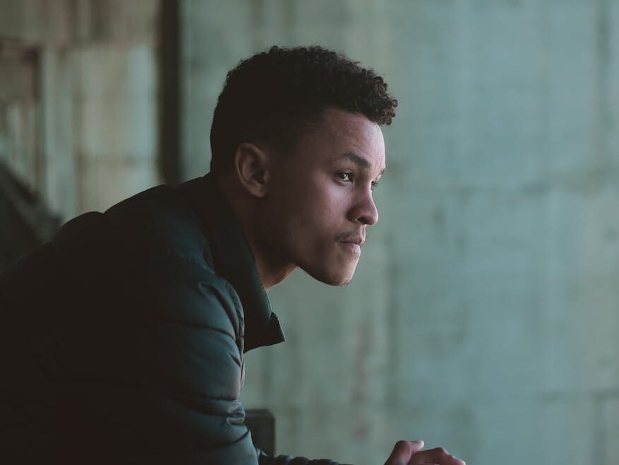 Young adult man leaning on metal railing looking pensive, wearing casual attire.
