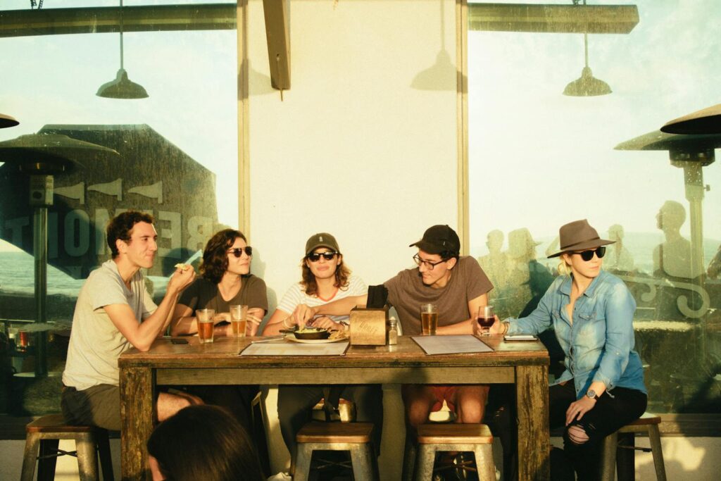 A group of friends socializing at a restaurant patio during sunset, sharing drinks and laughter.