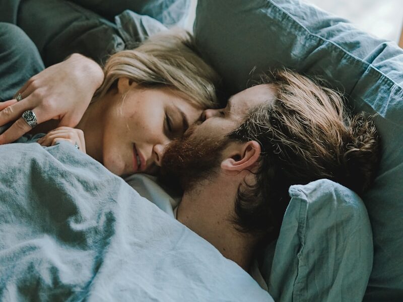 man kissing woman's forehead while lying on bed