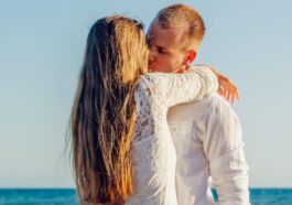 A couple sharing a romantic kiss by the ocean on a sunny day.