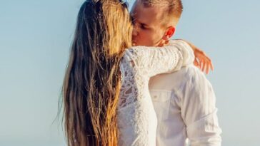 A couple sharing a romantic kiss by the ocean on a sunny day.