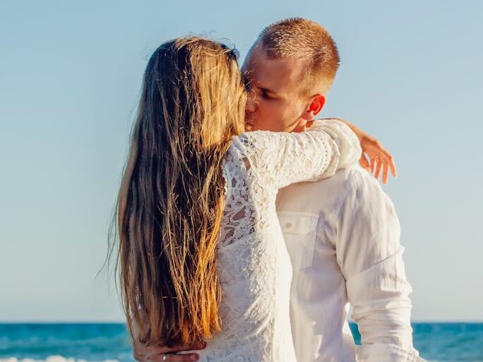 A couple sharing a romantic kiss by the ocean on a sunny day.