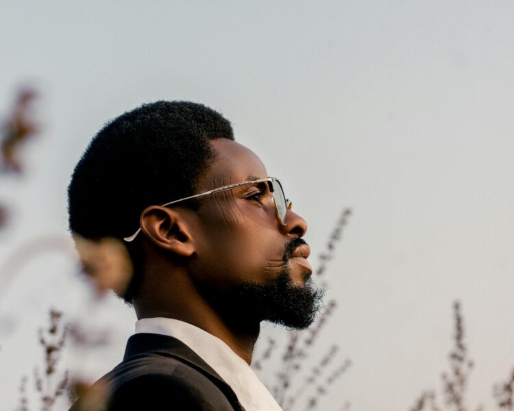 Portrait of a contemplative man gazing outdoors wearing glasses, against a blurred natural background.