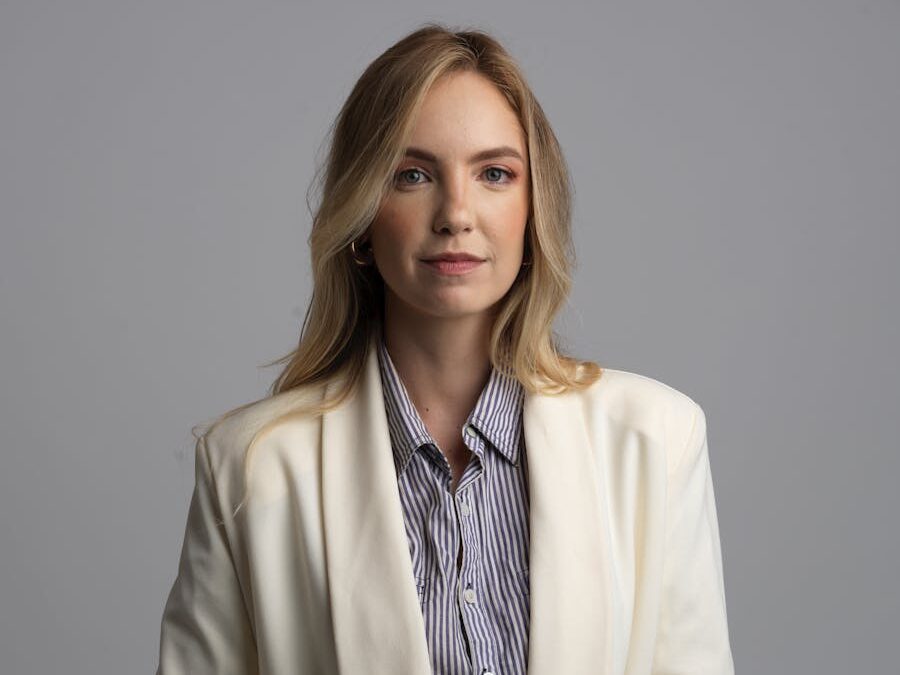 Elegant portrait of a woman in a white blazer with a neutral background, exuding confidence.