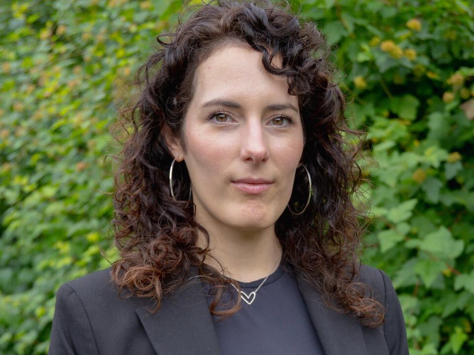 Confident woman with curly hair posing in a black suit outdoors.