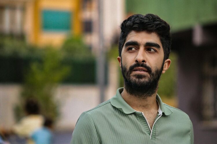 A thoughtful man in a green shirt gazing away, outside an urban setting.