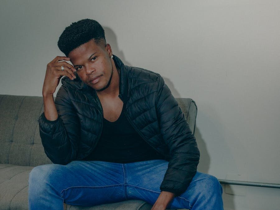Young man in casual clothes sitting on a sofa indoors, deep in thought.