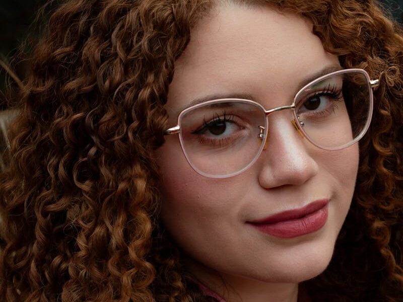 Close-up portrait of a woman with curly hair and glasses, showcasing natural beauty and style.