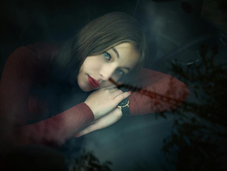 Emotive portrait of a woman gazing through a car window with a thoughtful expression.