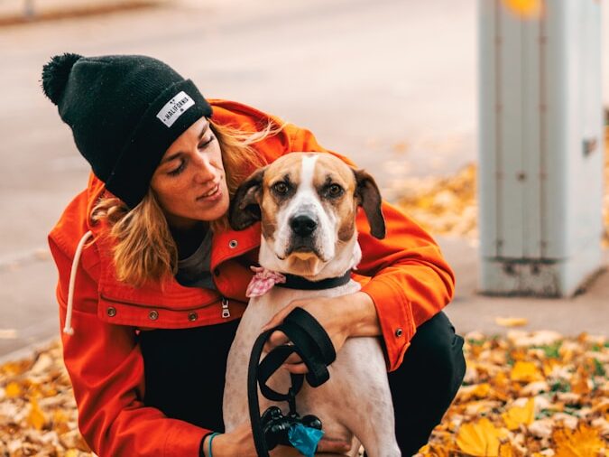 woman wearing orange jacket hugging brown dog