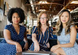 Three professional women sitting confidently in a modern office space, embracing diversity and collaboration.