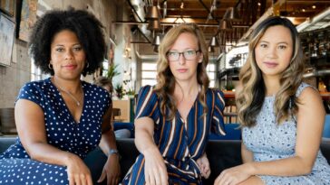 Three professional women sitting confidently in a modern office space, embracing diversity and collaboration.