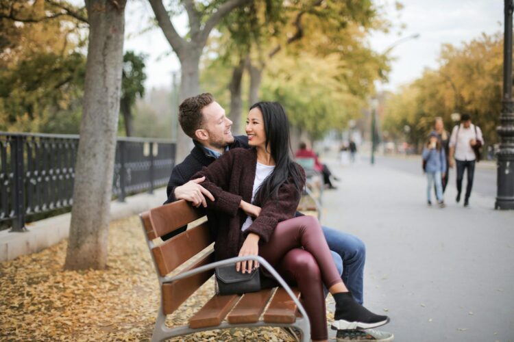 Happy couple sitting on a bench in a park during fall, sharing a joyful moment together.