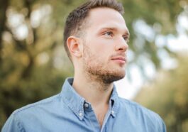 Portrait of a handsome young man with a beard looking thoughtfully in a sunny park setting.