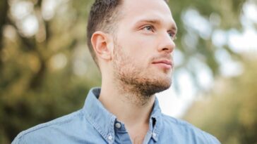 Portrait of a handsome young man with a beard looking thoughtfully in a sunny park setting.
