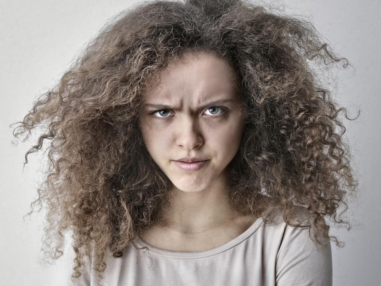 Portrait of a woman with curly hair showing an angry facial expression. Ideal for emotion-based content.