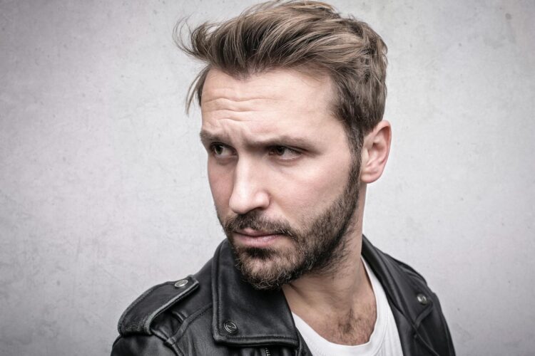 Close-up portrait of a bearded man in a leather jacket with a pensive expression.