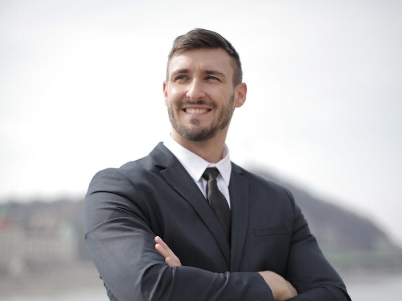 Smiling businessman in a suit standing confidently outdoors by the river.