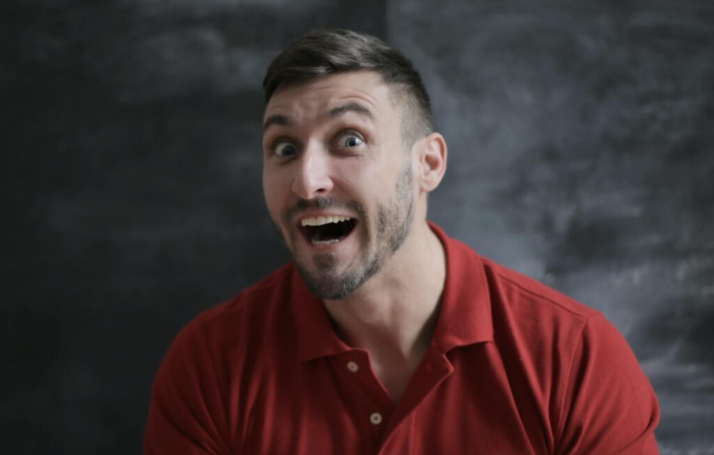 Close-up portrait of a man with a surprised expression wearing a red shirt.