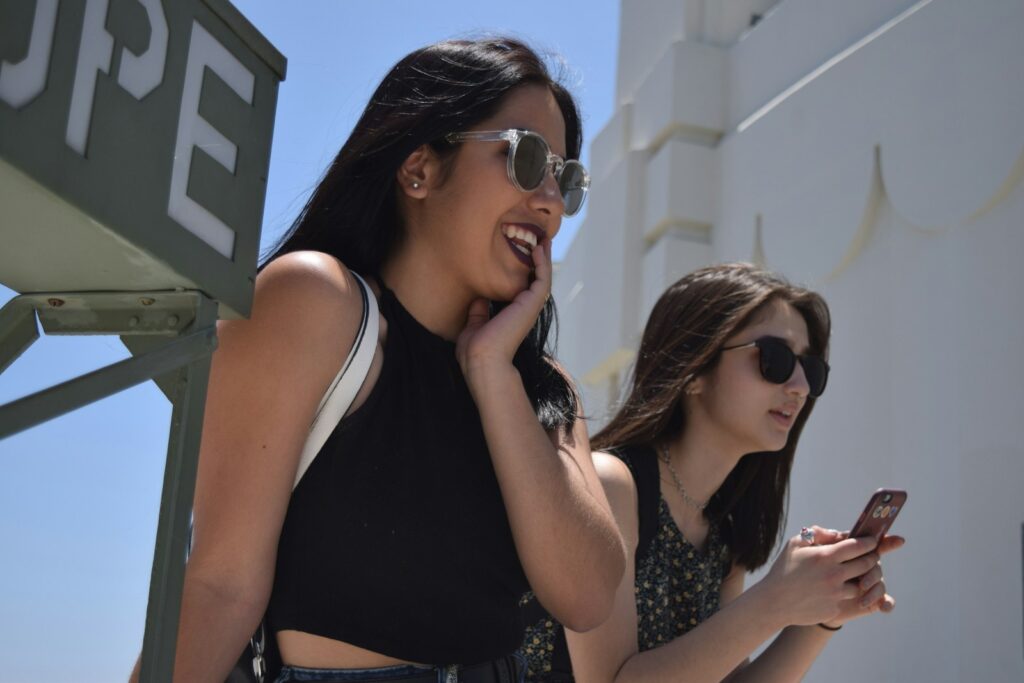 two women standing next to each other looking at their cell phones