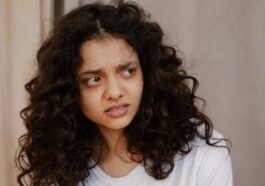 Portrait of a young woman indoors showing a confused facial expression with curly hair.