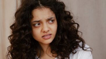 Portrait of a young woman indoors showing a confused facial expression with curly hair.