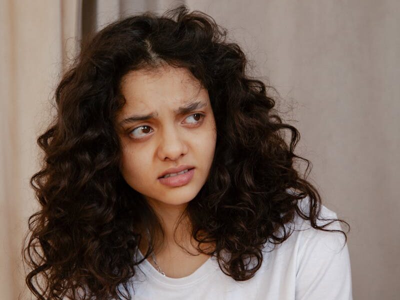 Portrait of a young woman indoors showing a confused facial expression with curly hair.