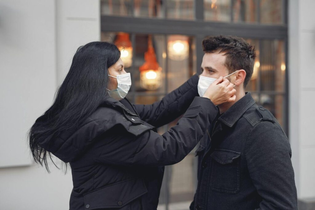 A woman adjusts a man's face mask on a city street, promoting health and safety.