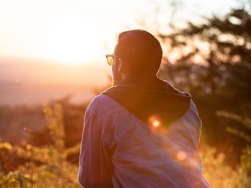 woman in white shirt and sunglasses sitting on brown wooden bench during sunset