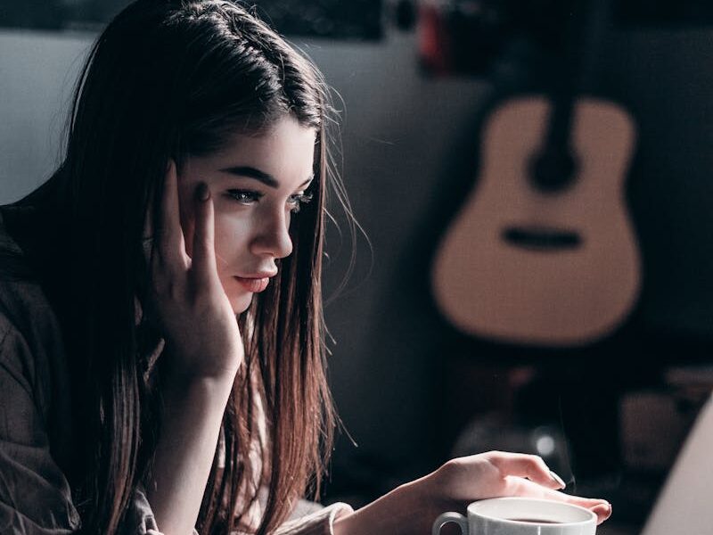 Woman lying on bed, focused on laptop with a coffee cup in hand, embracing remote work lifestyle.