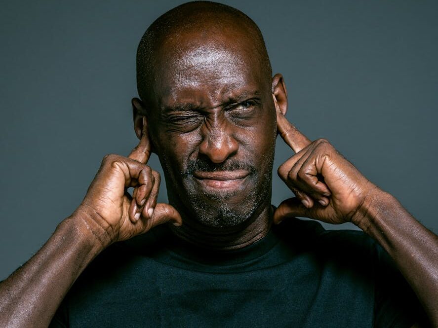 Portrait of a man blocking his ears to avoid loud noise, looking irritated.