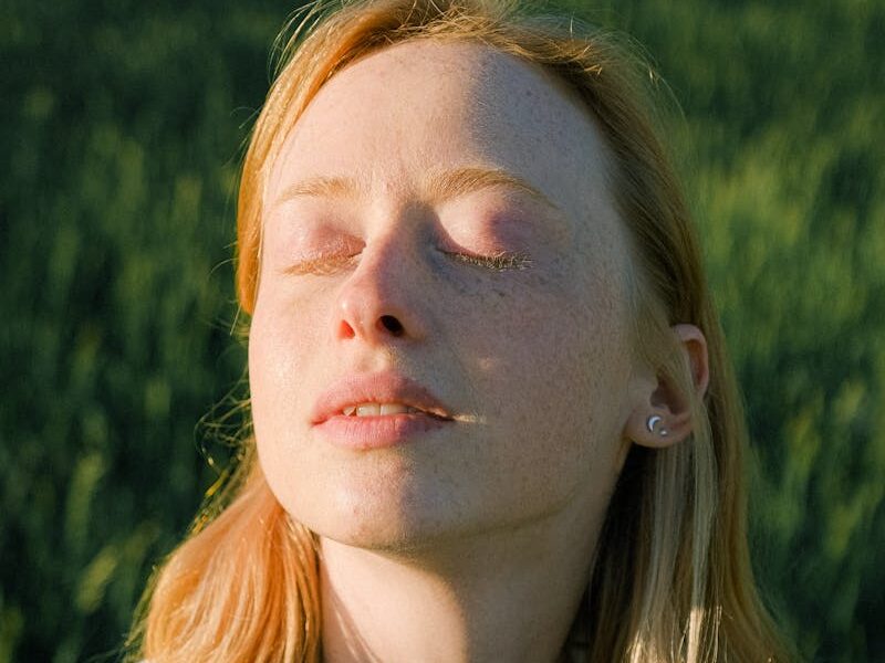 Tranquil portrait of a woman enjoying the sunlight in a grassy field.
