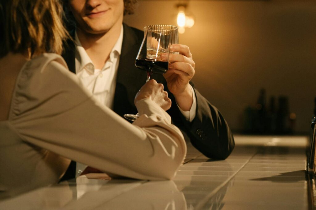 An elegant couple enjoying a romantic evening with wine toasts at a dimly lit bar.