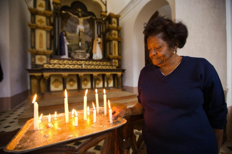 Senior woman lighting candles in a church, praying with hope and faith.