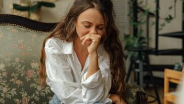 Woman in a white shirt sitting thoughtfully on a vintage sofa indoors.