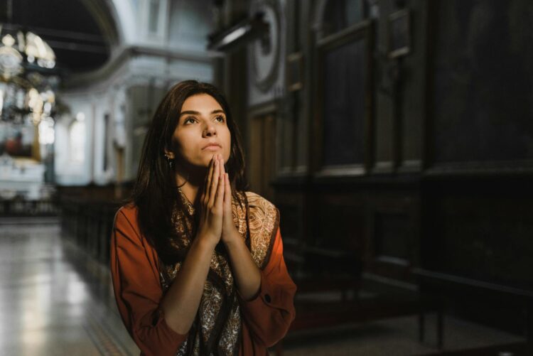 A woman is praying with hands clasped in a dimly lit church, creating a contemplative mood.