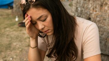 An anxious woman outdoors touching her forehead, showing stress and mental exhaustion.