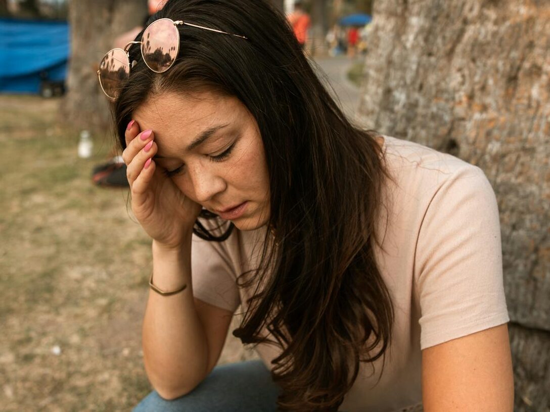 An anxious woman outdoors touching her forehead, showing stress and mental exhaustion.