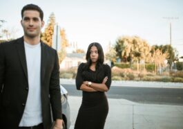 A couple facing relationship tension outdoors with arms folded, expressing emotions.