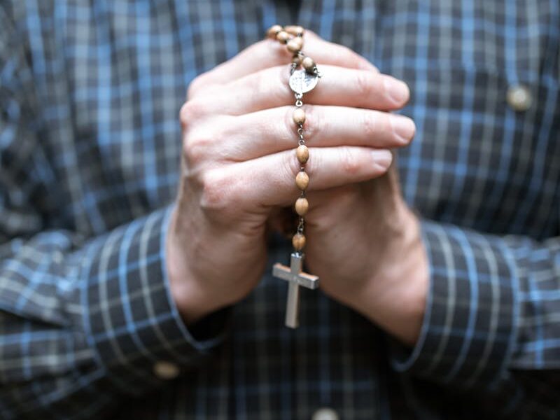 Close-up of a man holding rosary beads in prayer. Focus on faith and contemplation.