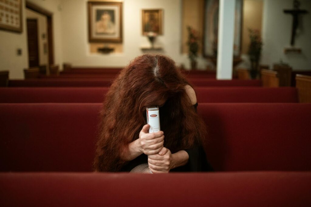 A woman with red hair prays intensely in a church pew, holding a bible tightly.