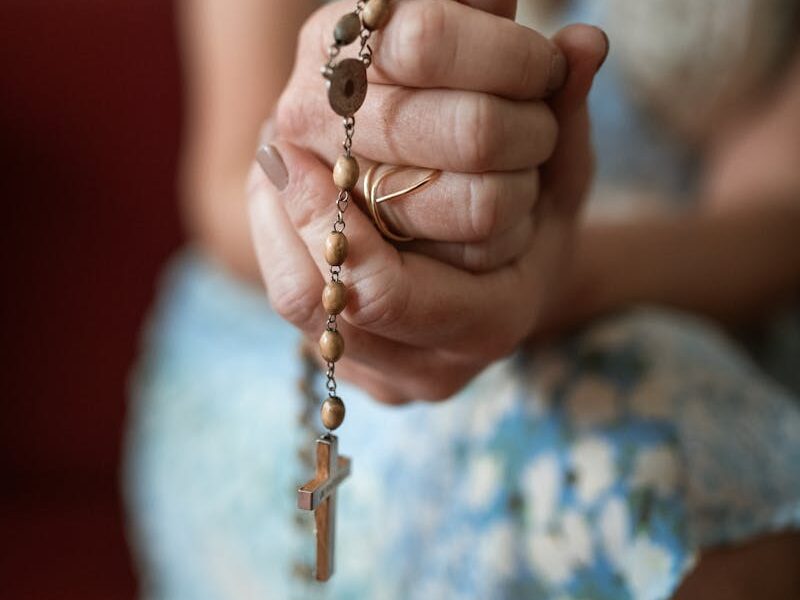 Woman's hands clasped in prayer with a rosary, symbolizing faith and devotion.