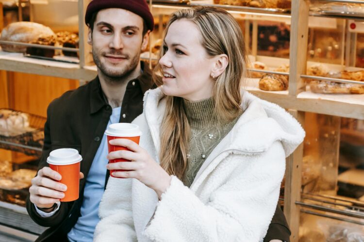 Positive young man and woman spending weekend in cosy bakery having hot drink