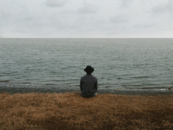 man in black and white checkered dress shirt sitting on brown grass field near body of near near near near